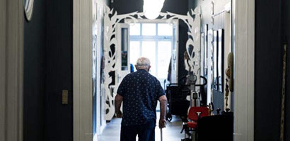 ældre herre går ned af gang med stok